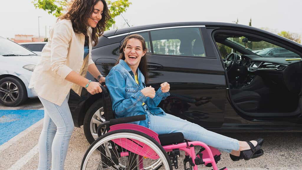 Very happy young woman in a wheelchair who is being pushed by a carer