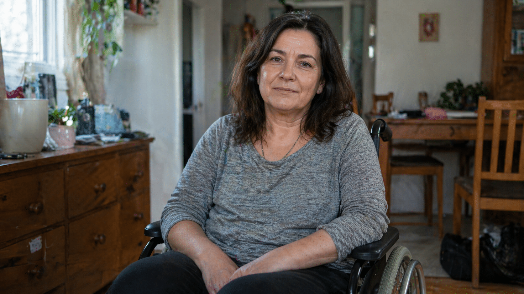 Middle aged woman sitting in a wheelchair at home, looking directly at the camera in a relaxed, natural setting