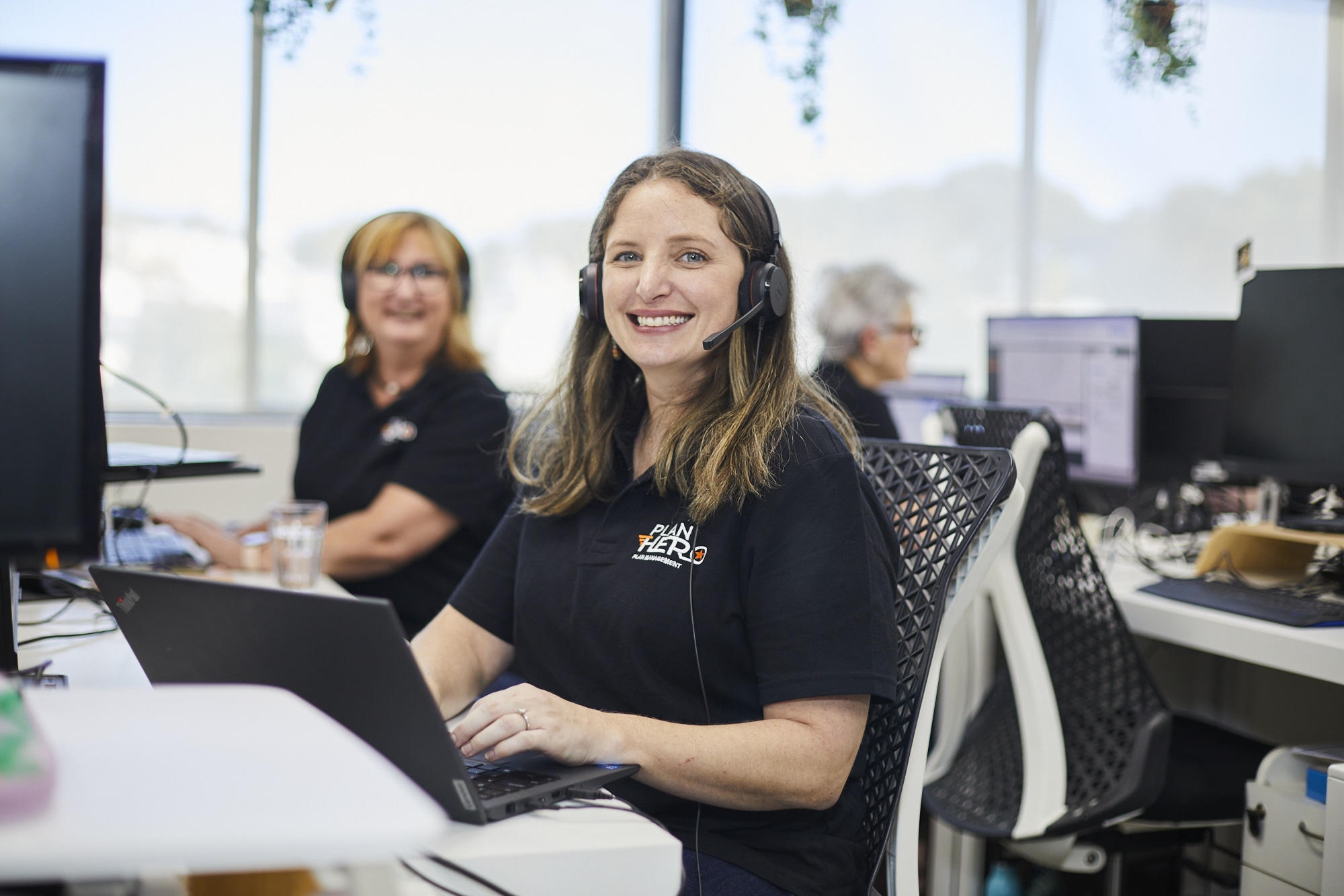 Plan Hero team member wearing a headset, smiling at her desk