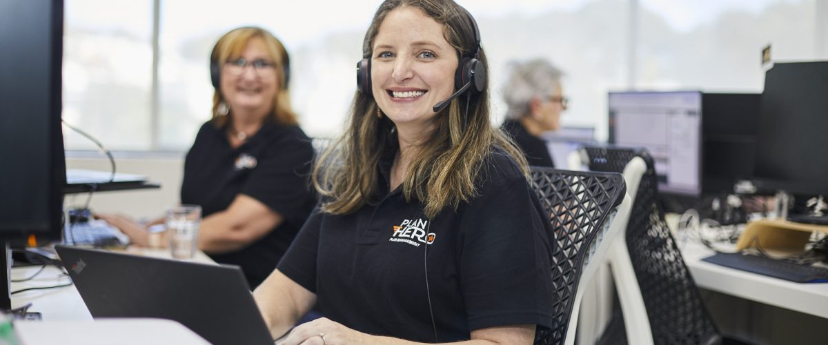 Plan Hero team member wearing a headset, smiling at her desk